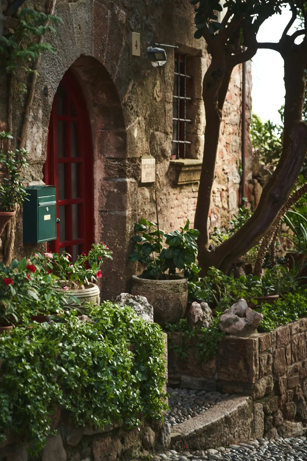 Casa rural de piedra con puerta roja rodeada de vegetación en Girona